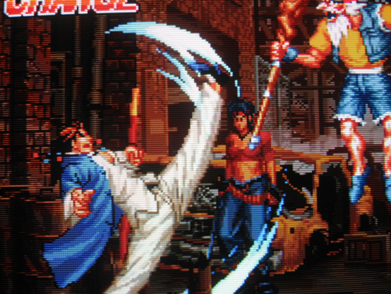 Kim Sue-Il performs a Chun-Li-esque overhead kick on a jumping old man who is wearing cut-off jean shorts. In the background Rosa is making a peeved face, impatiently.