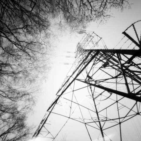 Looking up at an electricity pylon from the ground, with trees bearing in from the side