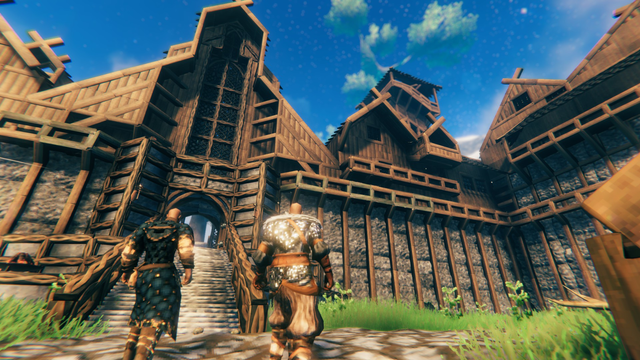 Valheim Screenshot: Two Vikings in front of a large building which appears to be part of a larger complex.