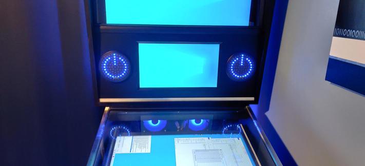 Picture of a virtual pinball cabinet with round speaker grilles with rings of LEDs behind them.  The LEDs are lit up in the shape of a power symbol (1 in 0), intended as a customization to a Tron table.