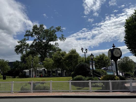 The image depicts a serene park-like setting with a large, ornate clock on the right side, featuring a black face and white numerals. The clock is mounted on a tall, decorative post. In the foreground, a white metal fence runs parallel to a brick-paved walkway, separating the viewer from the grassy area. The grass is well-maintained, with various trees and shrubs adding greenery to the scene. A few street lamps with black lampshades are visible, contributing to the park's aesthetic. In the background, there are buildings with dark roofs, and a large tree with a wide canopy stands prominently. The sky is partly cloudy, with patches of blue visible, suggesting a pleasant day. The overall atmosphere is calm and inviting, with a focus on the clock as a central feature.

Provided by @altbot@fuzzies.wtf, generated privately and locally using Ovis2-8B

🌱 Energy used: 0.212 Wh
