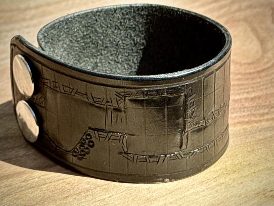 A leather wrist cuff with nickel snaps. It has a tooled texture that is reminiscent of old school D&D dungeon maps.