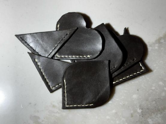 An assorted pile of dark grey leather page corner bookmarks in various shapes, some with white linen thread, some with black.