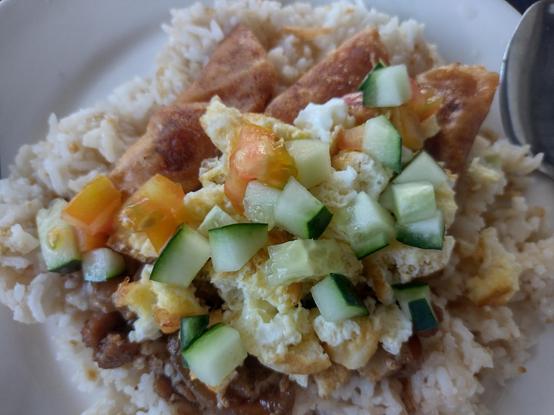 Closeup of Pork Budbod (meaning "sprinkled"). Fried rice topped with small cuts of pork, spring rolls, tomatoes, and cucumbers