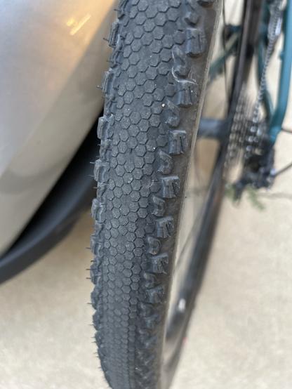 Close-up view of a bicycle tire, showcasing its textured surface and tread pattern, with a blurred background of a vehicle.