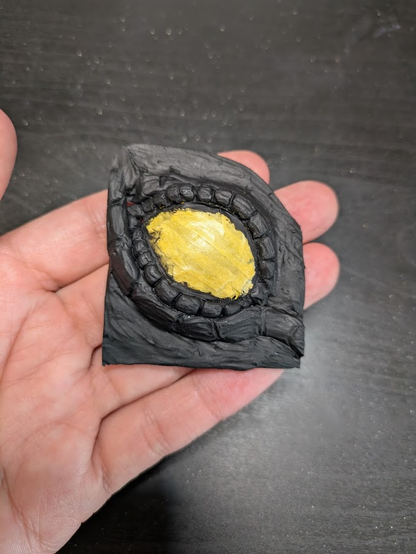 The dragon eye insert. The skin and scales are black primed, and the eye is covered in yellow masking tape.