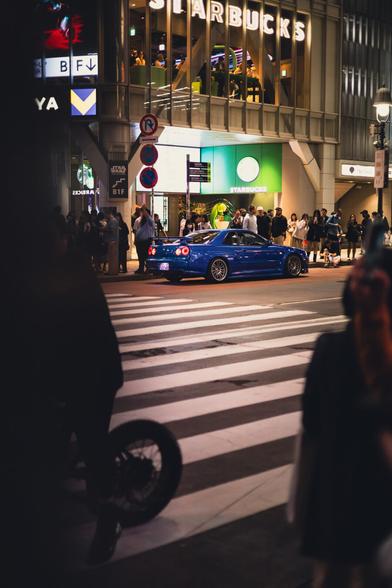 photo of a blue Nissan Skyline R34 tuning car standing near the famous Shibuya crossing in Tokyo, Japan