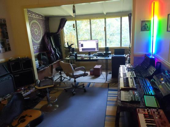 A room filled with synthesisers, guitars and amps, and other assorted paraphernalia.