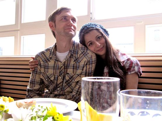 Man and woman cuddle at a table with a window behind them.