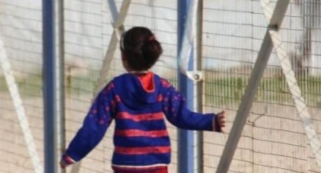 Une enfant derrière les grilles d’un camp.