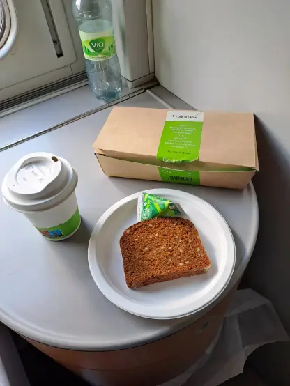 Photograph (colour): A take away mugg, a sluce of bread on a paper plate, a brown paper box