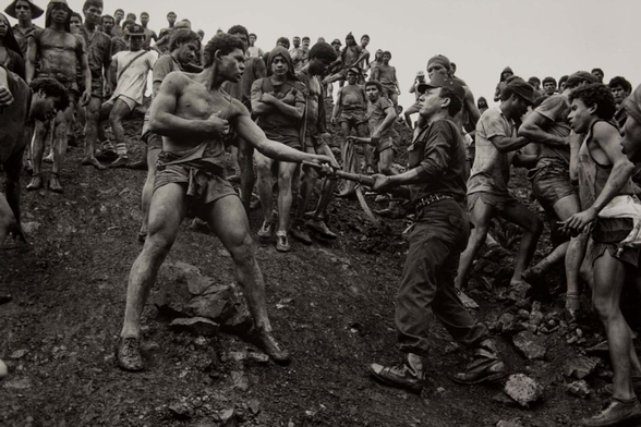 Untitled, Serra Pelada, Brazil
1986  · gelatin silver print
Sebastiao Salgado  ·

A shirtless worker bravely grabs the muzzle of a gun pointed at him by a uniformed mercenary, before a crowd of other workers.