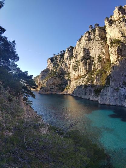 Arrivée sur la calanque d'en vau, elle est encore dans l'ombre mais le soleil du matin éclaire les falaises bien verticales orientées nord-est sur la droite de la photo.

L'eau de la calanque est bleu turquoise, on voit le fond très clair là ou il n'y a pas d'algues, et plus foncé partout ailleurs.

Sur la gauche de la photo on voit la végétation et les pentes de l'autre côté de la calanque.

Le paysage est idyllique, voir paradisiaque !

Le ciel est parfaitement dégagé et bleu.