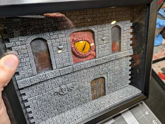 A loose fit of the painted floor and wall, with door and dragon eye, in the black diorama frame. It's held in hand.