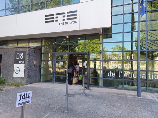 Photographie numérique couleur en format paysage.
Façade de l'institut français de l'éducation de l'École nationale supérieure, avec un panneau JdLL devant.