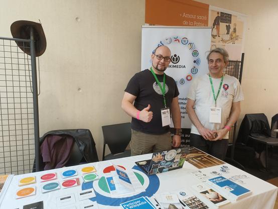 Le stand de Wikimédia France avec des affiches et des stickers. Derrière le stand, Lucas Lévêque et un membre d'Open street map.