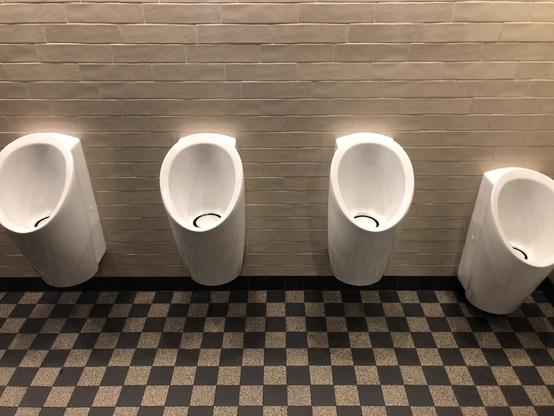 Herrentoilette mit vier Pissoirs. Die ersten drei hängen auf derselben Höhe, das vierte etwas tiefer.