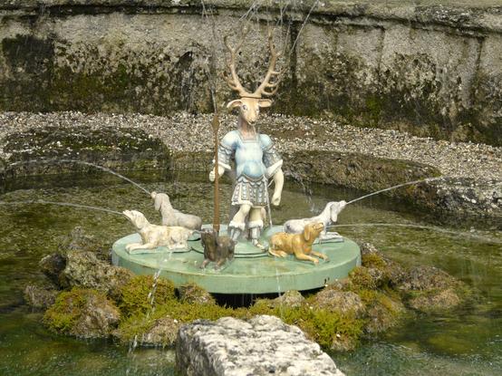 Eines der vielen außergewöhnlichen Wasserspiele auf Schloss Hellbrunn
Mittig in einem gemauerten Brunnen eine menschenähnliche Figur mit Hirschkopf und Geweih,
drumherum sechs Wasser speiende Jagdhunde