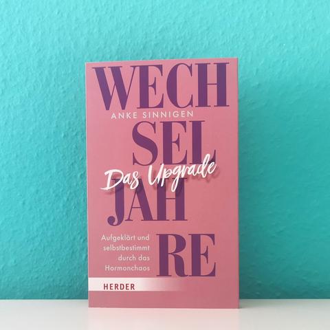 Auf dem Foto ist das Buch "Wechseljahre. Das Upgrade" zu sehen. Es steht vor einer türkisen Wand auf einer hellen, glatten Oberfläche.