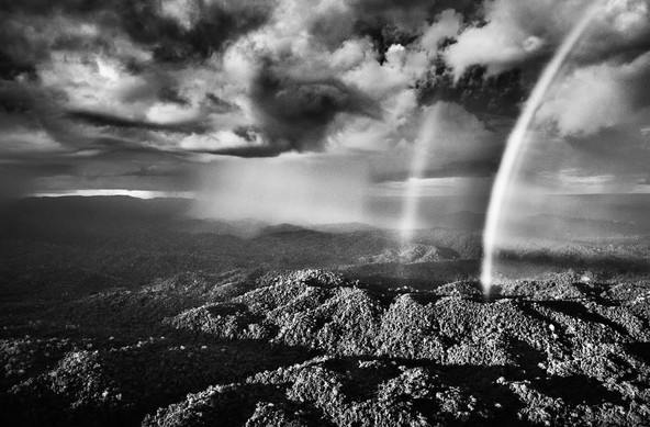 Stunning black and white photograph of the forest reserve, we see hills full of lush trees and spectacular clouds