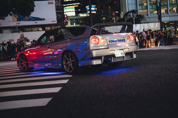 photo of the back of a silver Nissan Skyline tuning car with blue stripes known from Fast & Furious, on the Shibuya crossing in Tokyo