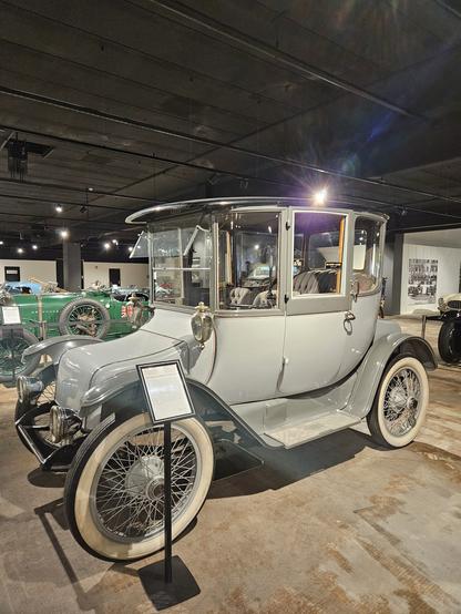 Light grey oldtimer with chrome finishing and spokes and laterns. It looks a bit like an horse carriage.