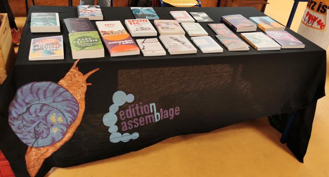 Büchertisch der edition assemblage, Tisch mit schwarzer bunt bemalte Tischdecke Auf der verschiedene Bücher liegen