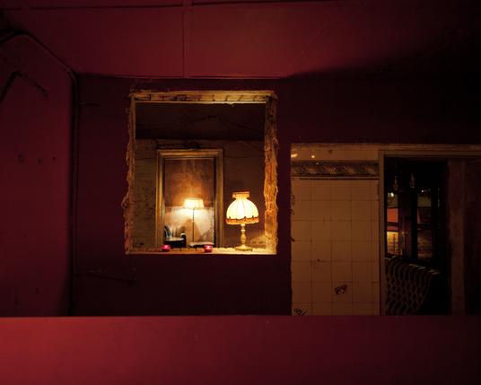 photograph of a old fashioned lampshade in a gloomy bar. the light it very warm, and the walls a deep red.