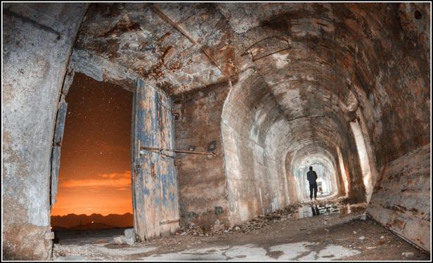 Une galerie de béton dans un ancien fort. À gauche par une porte entrouverte, l'on aperçoit une chaîne de montagnes.