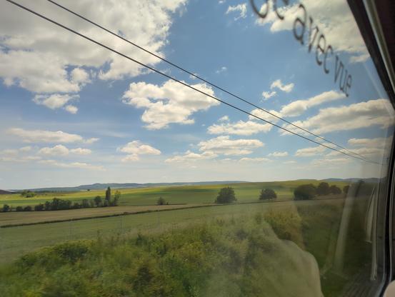 Photo prise dun TGV qui montre un paysage avec nuages blanc sur fond de ciel bleu et champs verdoyants non sans rappeler le fond d'écran par défaut de Windobe