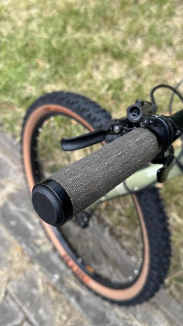 Nahaufnahme eines Fahrradlenkergriffs und Bremshebels, mit einem verschwommenen Hintergrund mit einem Teil eines Rades und Gras.