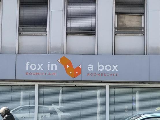 A store front with the window shutters closed inside. It reads fox in a box, roomescape, with a minimalistic fox logo