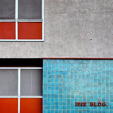 Midcentury building with a light blue tile facade and an orange sign that says 1919 BLDG. to the left are some windows with colored panels in that same orange.