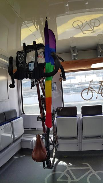 Vélo de rando accroché dans un TER avec un drapeau des fiertés roulé et rangé le long du tube supérieur