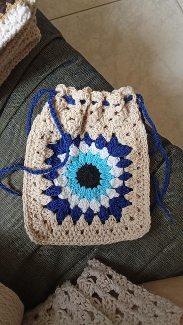 Fotografía de saco pequeño tejido a crochet con una imagen de ojo azul en el centro y cintas azules para cerrar.