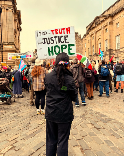 Girl with her back to viewer holding protest sign which says “I stand for truth, for justice and for hope” with protesters in front of her