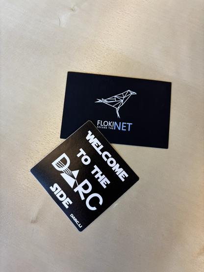 One business card from Flokinet and a sticker from DARC lay next to each other. The sticker reads “Welcome to the DARC side”