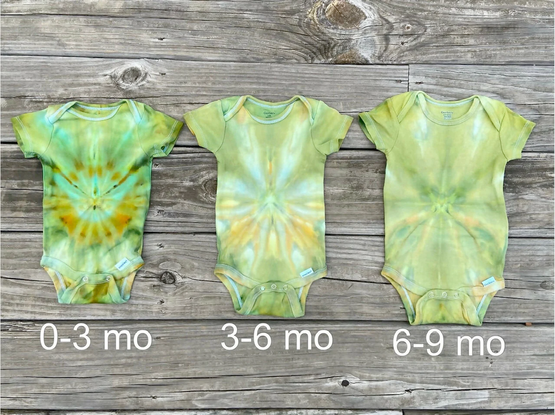 Photo of three baby bodysuits tie dyed in greens and yellows. Photo is labeled with the sizes the suits are available. 0-3 months, 3-6 months, and 6-9 months.