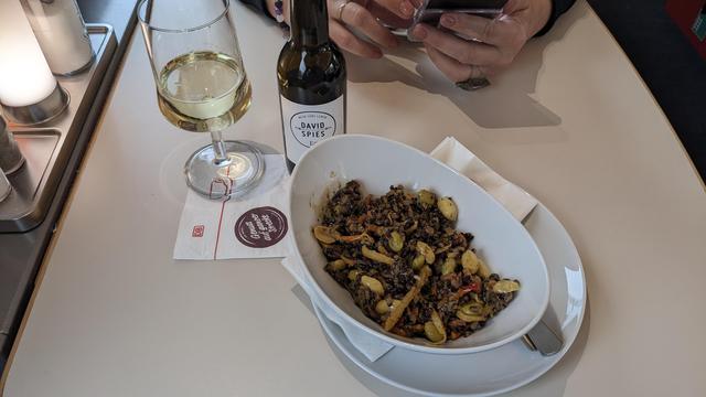 A plate with dark rice salad next to a glass and a tiny bottle of white wine.