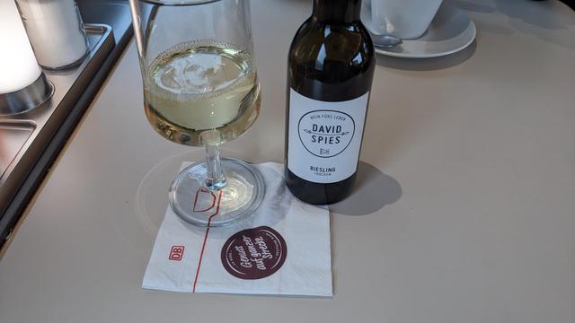 A bottle of Riesling wine next to a half filled glass on a dining car table.