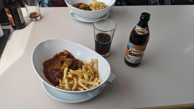 A dining car table with two plates of Vegan Curry Sausage and two Spezi lemonades.