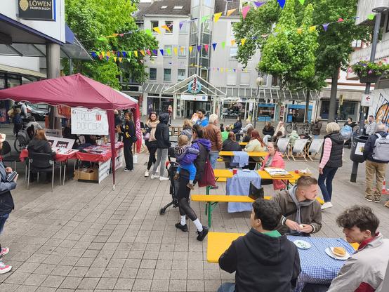 Straße, bzw. Fußgängerzone mit etlichen Tischen und Bänken und einem Roten Pavillon an dem "Free Popcorn" steht.