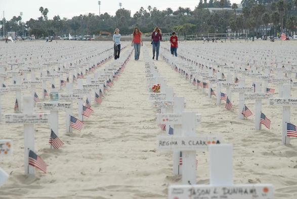Four people walk on a beach down separate rows made from crosses. Each one marks a soldier who has died.