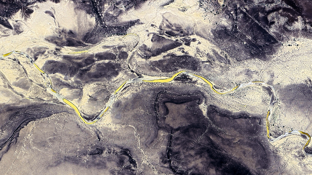 a satellite picture of a grey desertic landscape with a yellow river winding though it from left to right