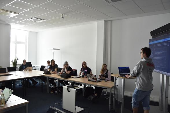A group of people in a conference room, listening to the speaker and trying things out on their laptop.