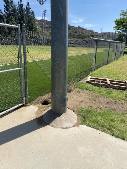 Park privatization! The city is forcing the private maintenance company to rehabilitate the fields for the leagues (and taxpayer via city budget) paying fees, this is how they left the fence. Image shows a metal light poll next to a chain link fence that has been shoddily repaired and wooden pallet off to the side of the broken fence.