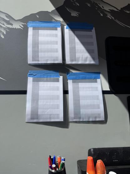 Four laminated 8.5x11” sheets of paper taped to the side of our RV with blue painter’s tape

They’re arranged in a 4x4 grid. The sheets each have a spreadsheet-style gray and white grid printed on them to help keep writing tidy 

At the bottom of the image is a cup full of dry erase markers