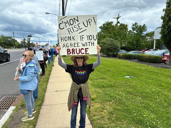 A protester stands by the roadside in New Jersey holding a sign that reads "C'mon Rise Up! Honk if you agree with Bruce," surrounded by fellow demonstrators. Image by ‪Pammie‬ ‪@swtseastar.bsky.social‬