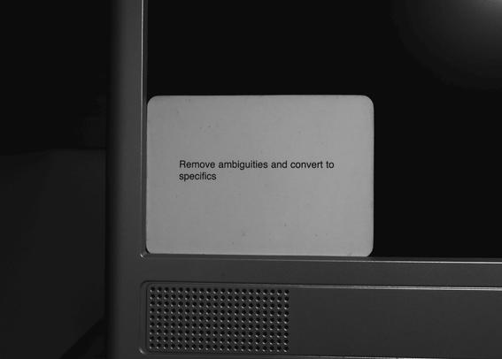 A black-and-white photo of an Oblique Strategy card. The card reads: 'Remove ambiguities and convert to specifics'.