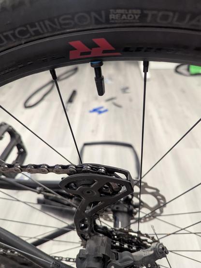 Foto durch das Hinterrad von einem Fahrrad aufgenommen.
Im Vordergrund ein Tubeless-Ventil und Teile vom Reifen und der Schaltung.
Im Hintergrund ein Fahrradschlauch und verschiedenes Werkzeug.